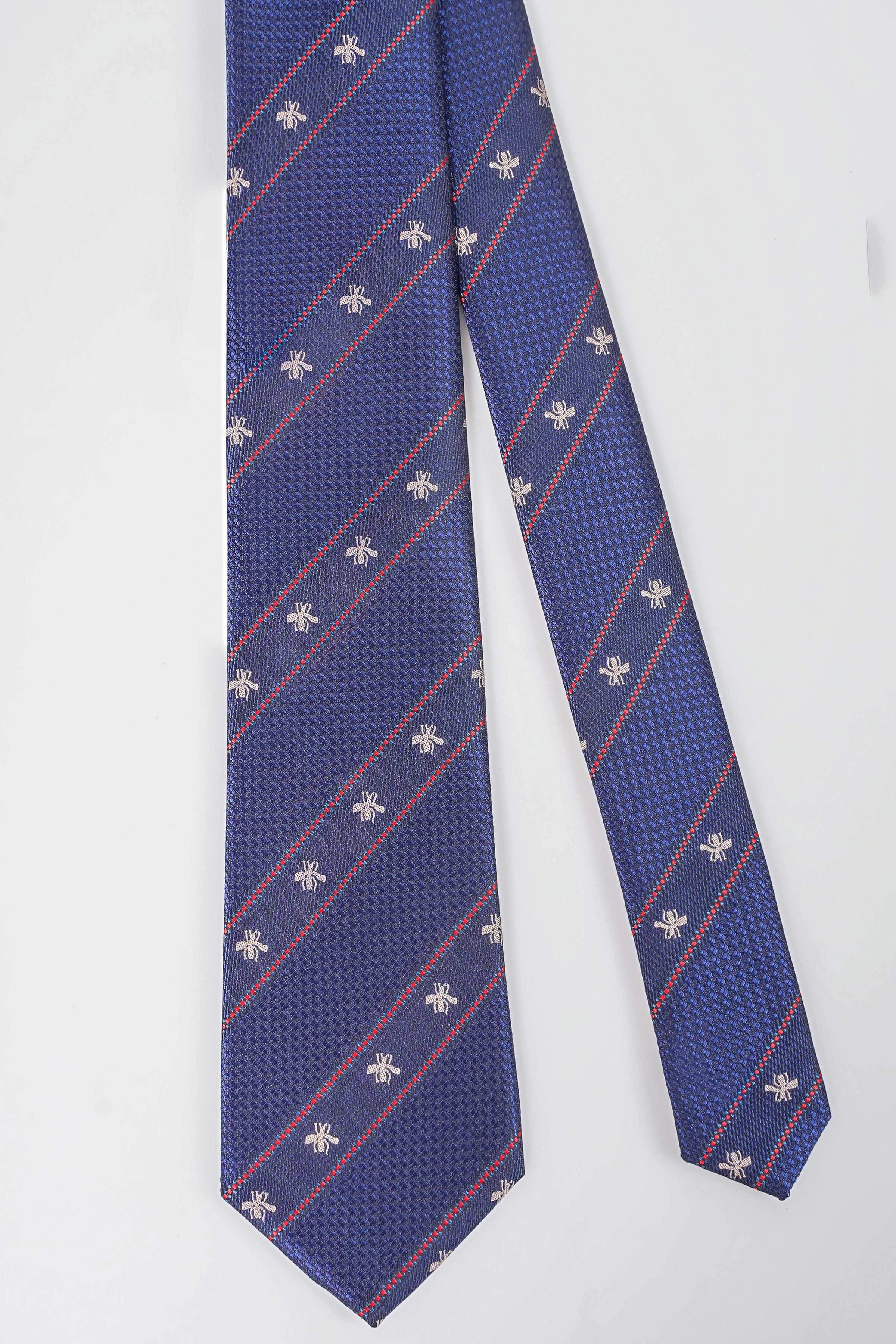 Blue poly silk tie with diagonal red plaid lines and repeating fleur-de-lis motifs