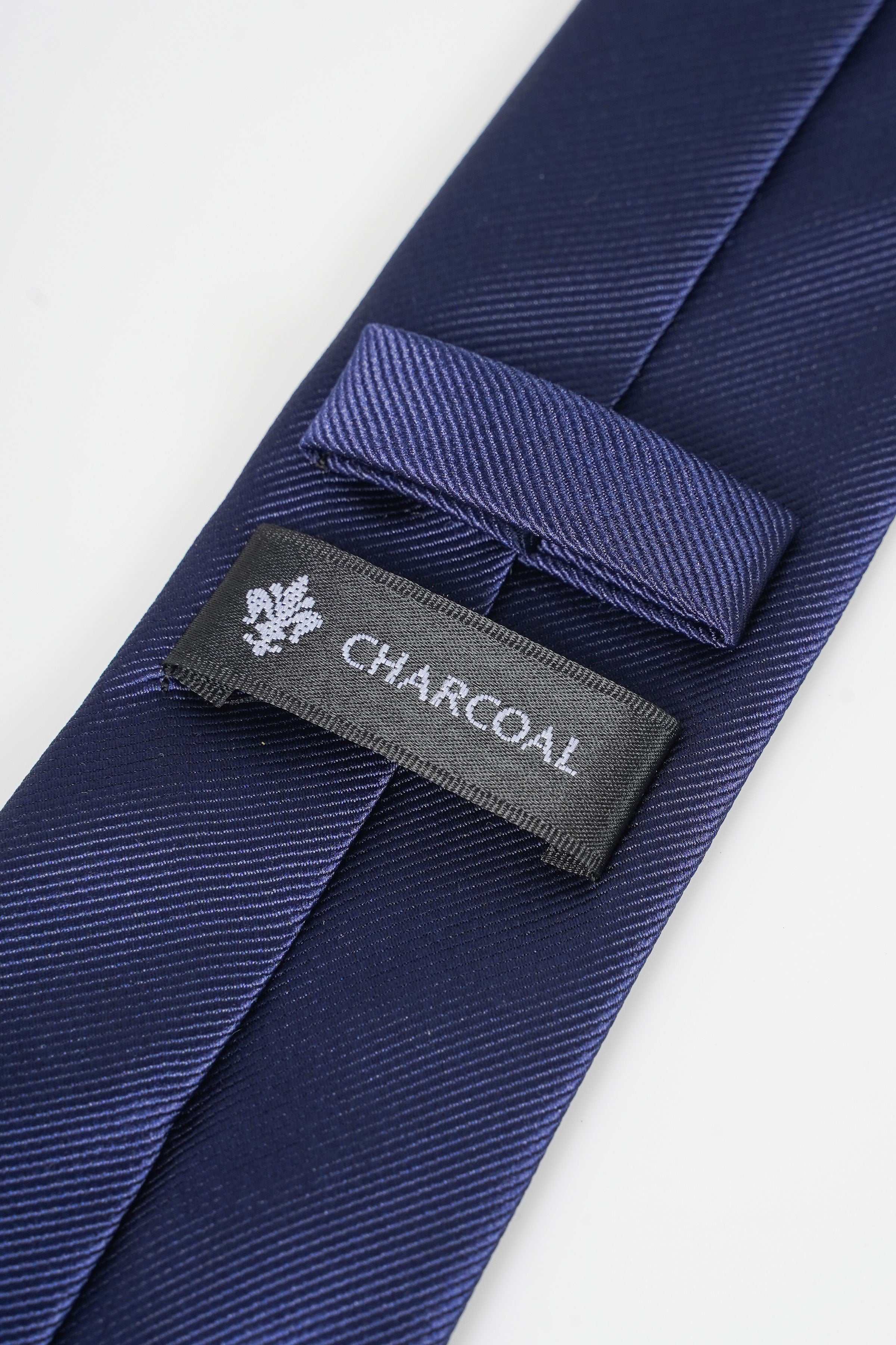 Poly silk tie with CHARCOAL label and small emblem on dark-blue fabric.