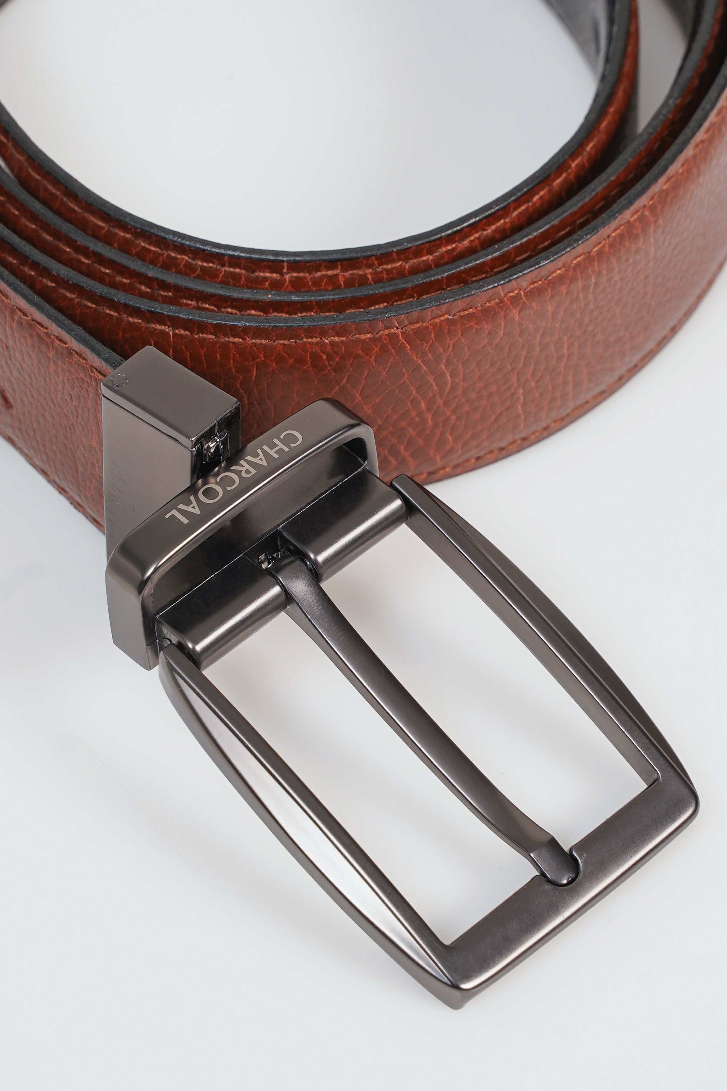 Reversible belt buckle detail with metal keeper on brown leather strap