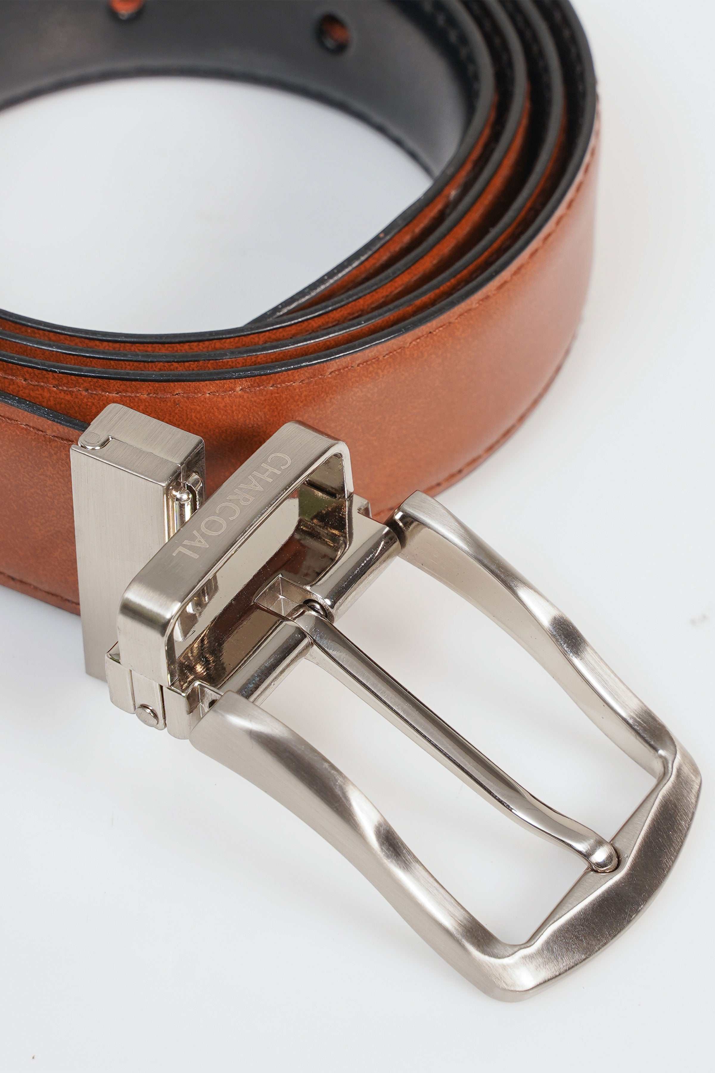 Reversible belt buckle close-up on brown leather strap with multiple holes