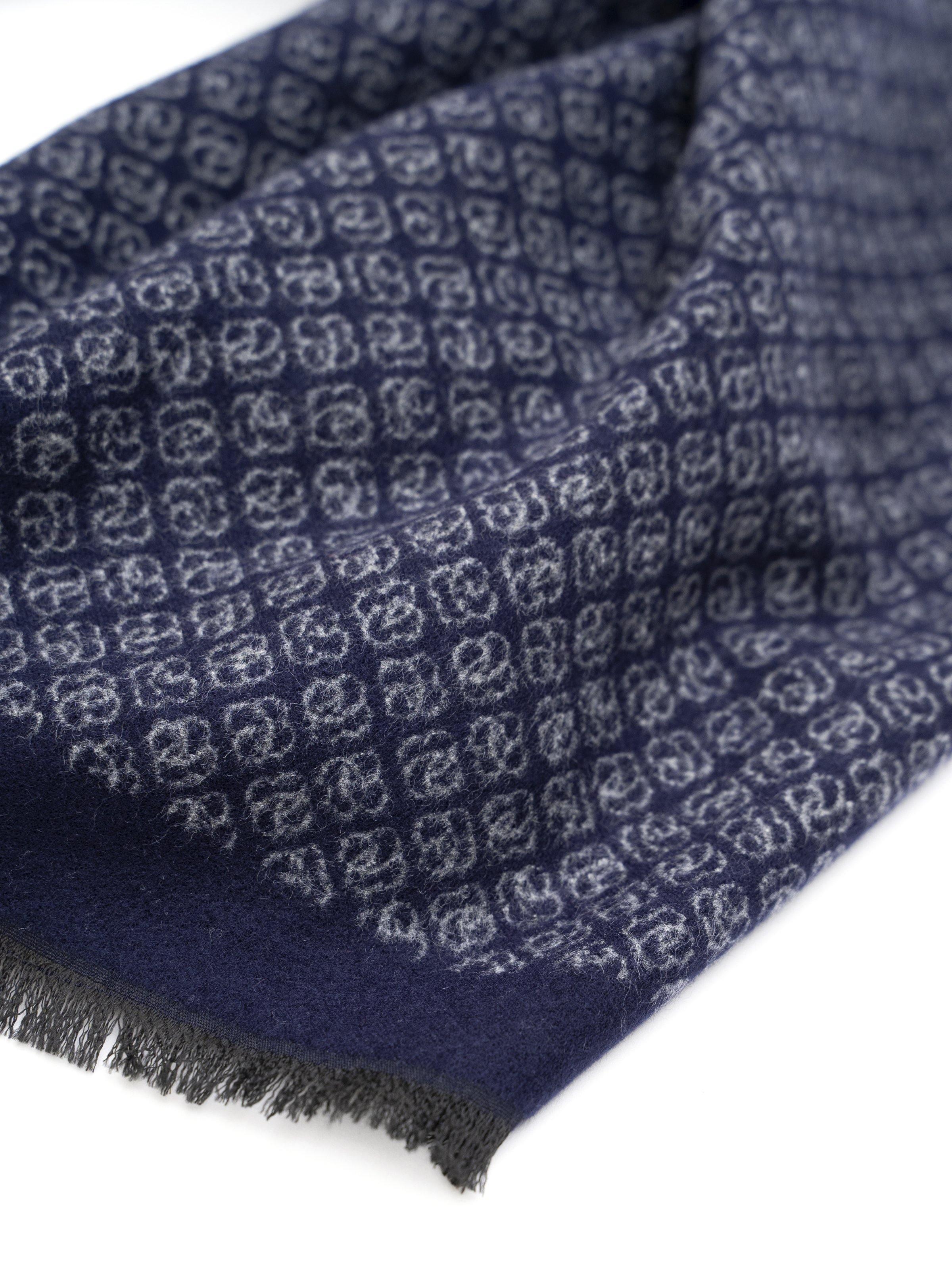 Navy scarf close-up with repeating motif and frayed fringe corner.