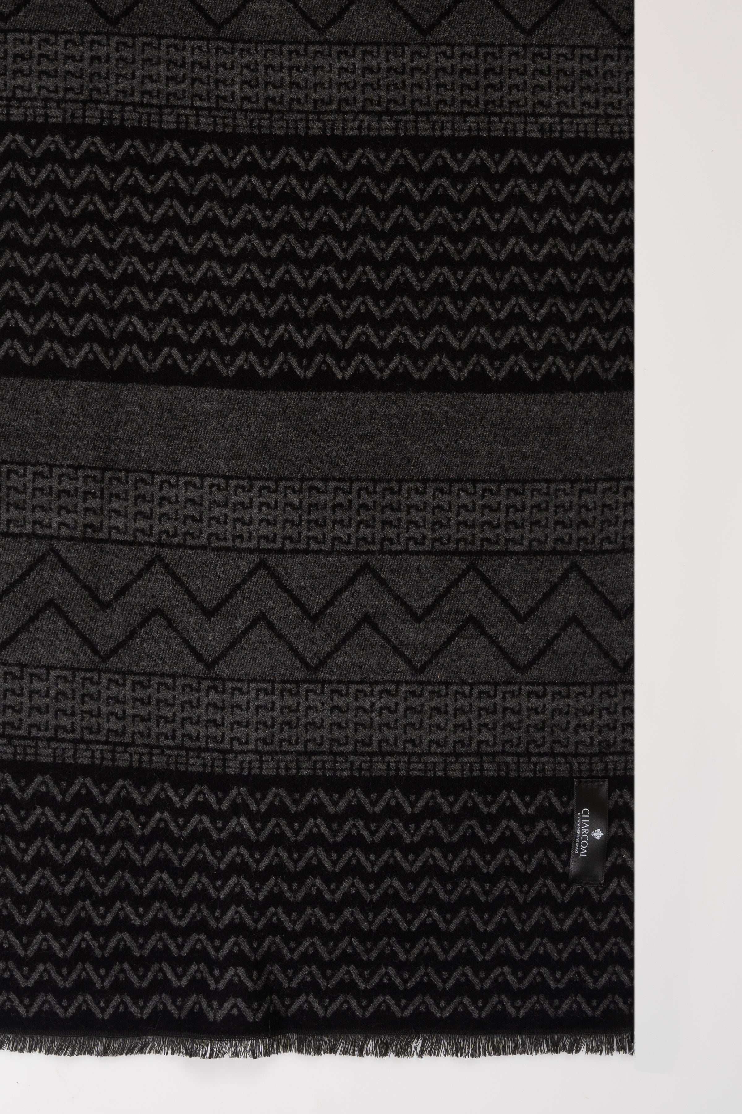 Dark patterned scarf close-up with zigzag bands and stitched border, with fringe edge