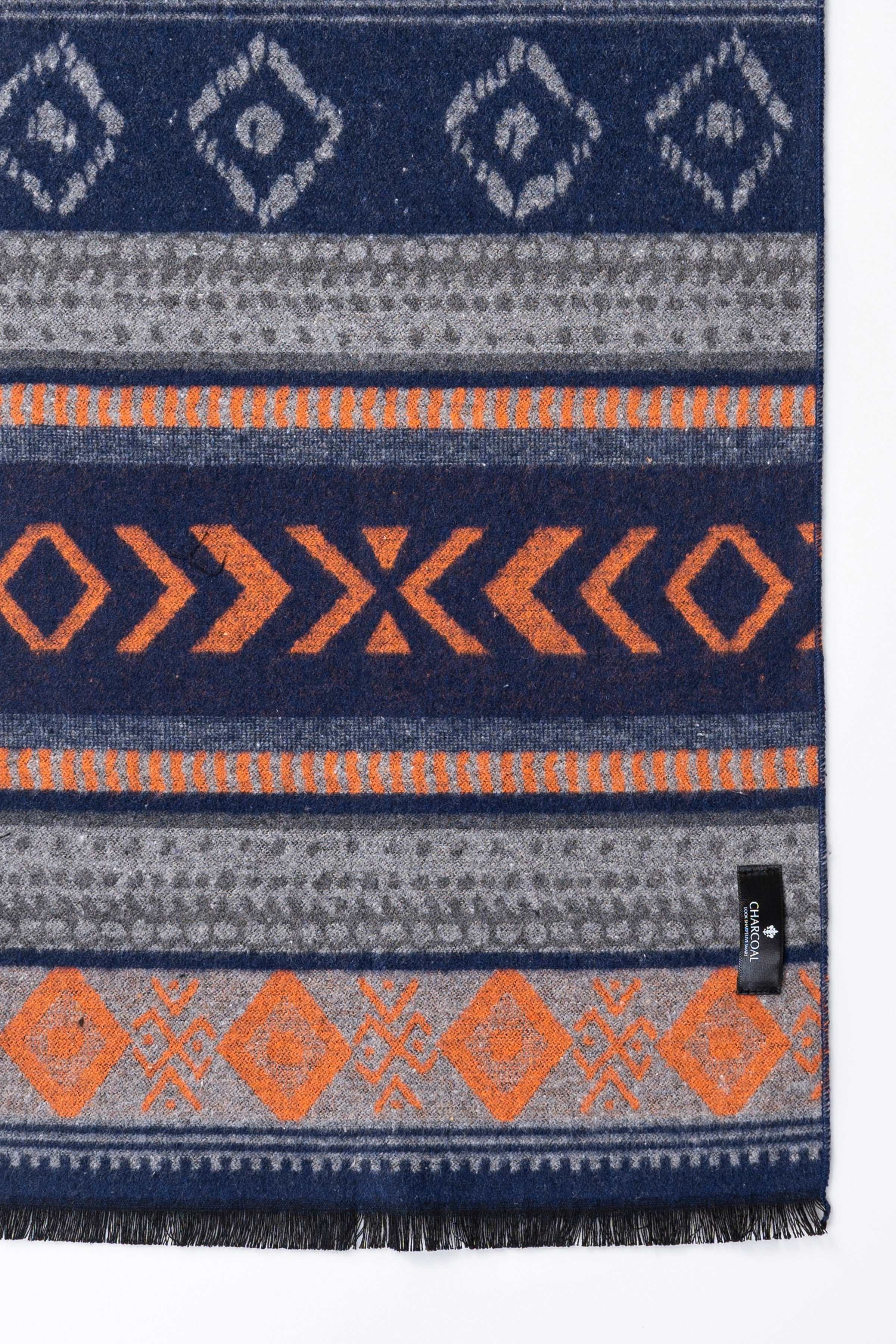 Navy scarf close-up with geometric motifs, orange zigzags, and black tag at hem