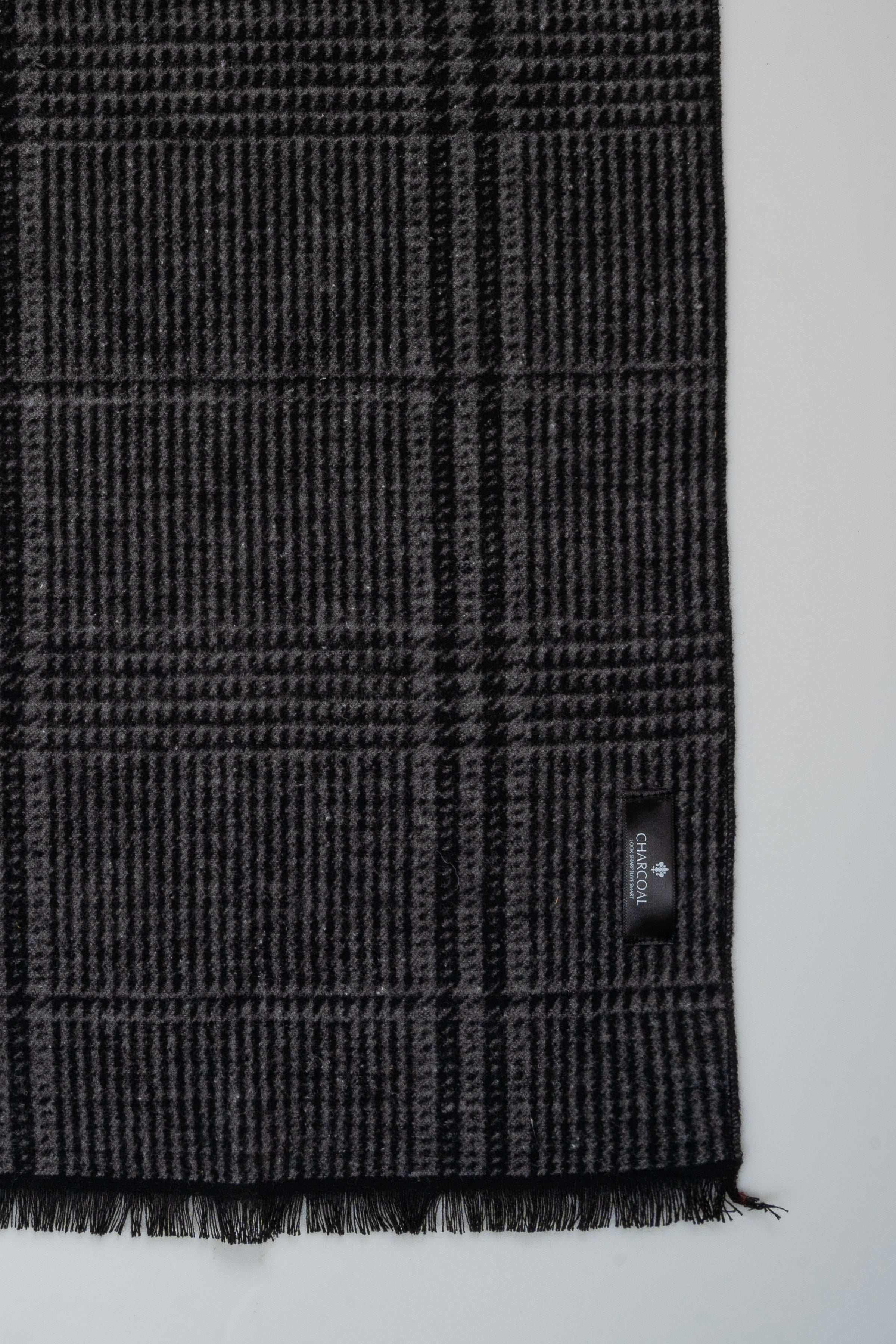 Charcoal plaid scarf fabric close-up with stitched hem and logo label; fringes