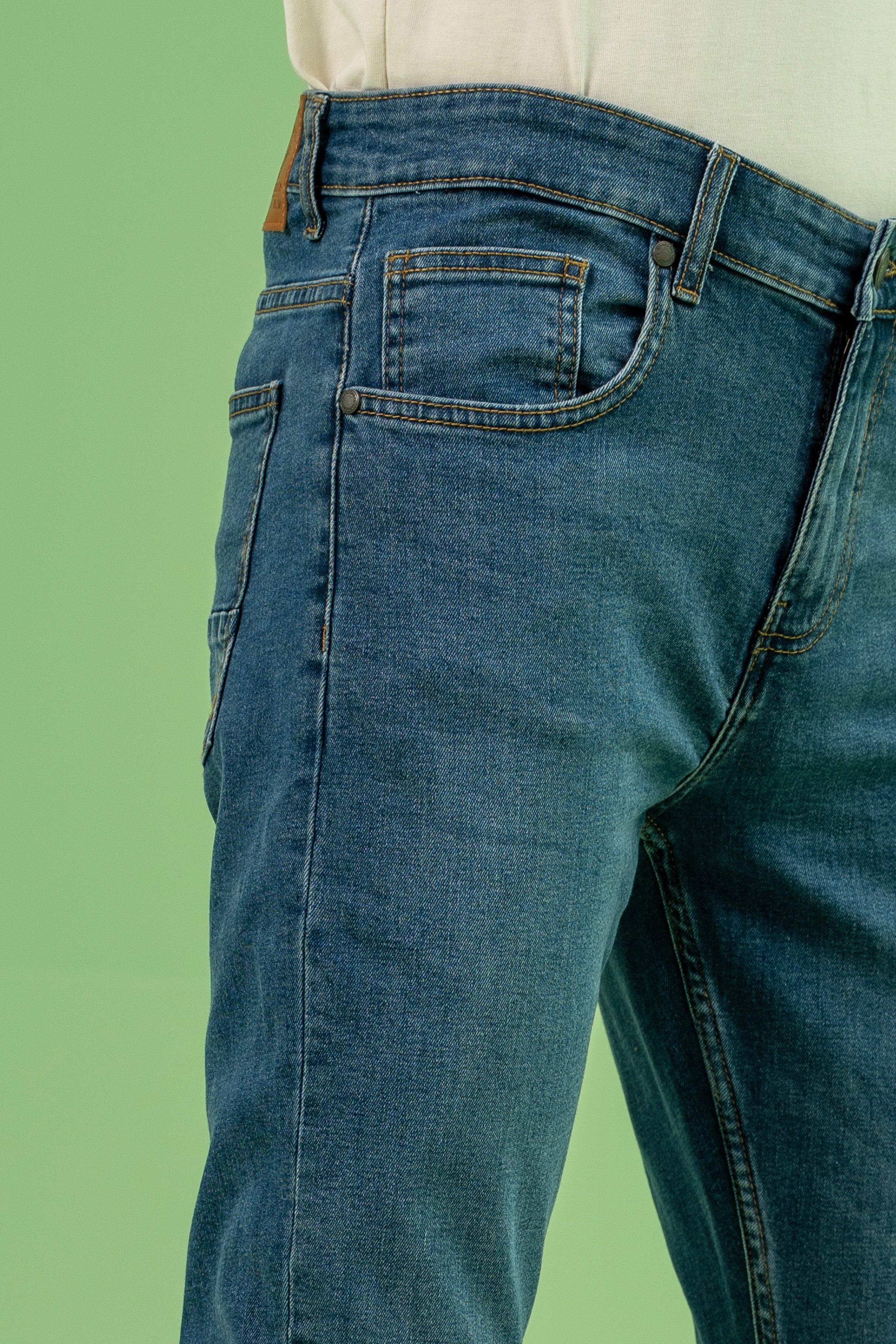 Mid-blue denim jeans close-up: curved front pocket, belt loops, stitched seams