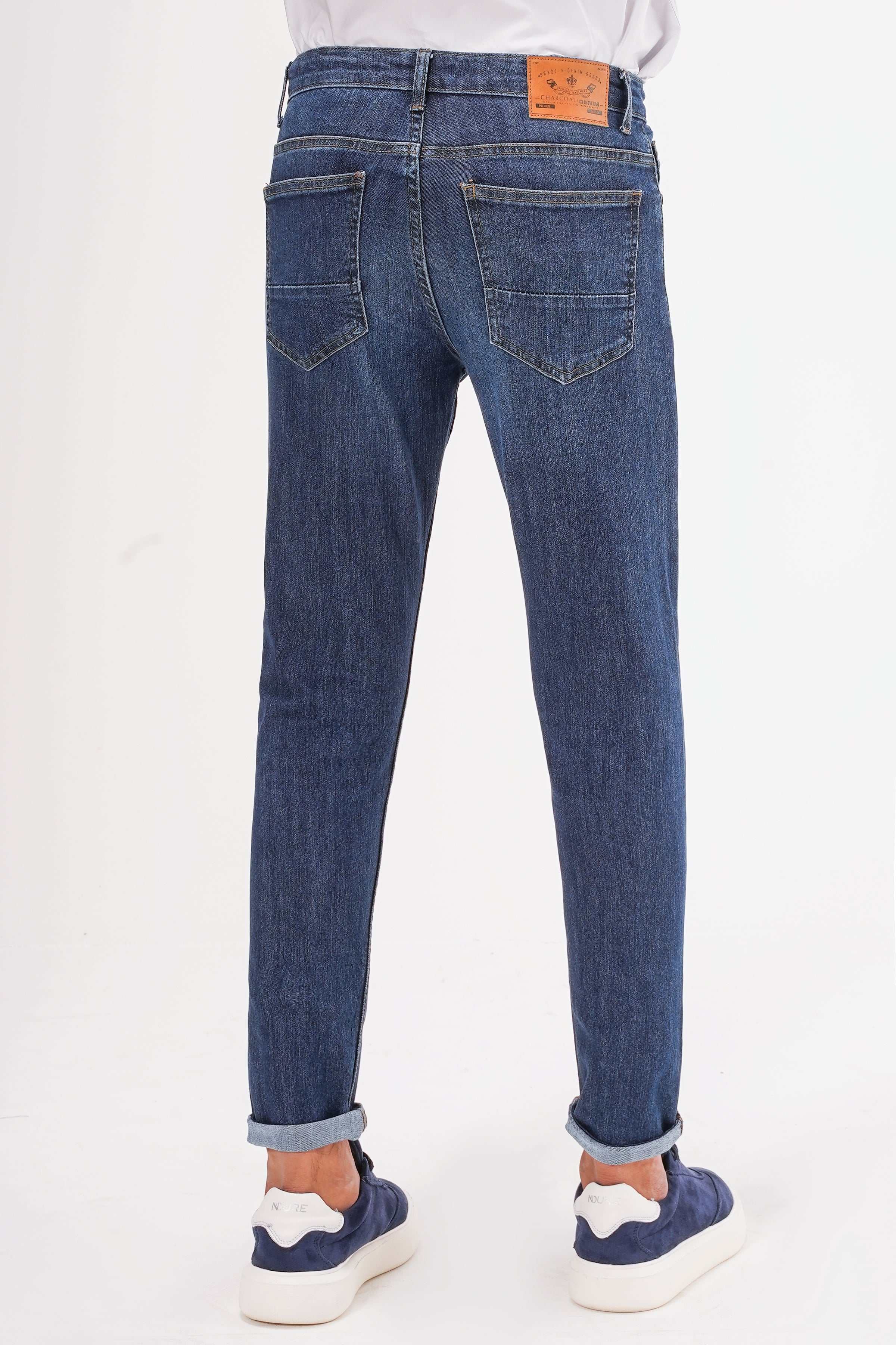Dark blue slim-leg jeans back view with orange logo patch, belt loops, two back pockets