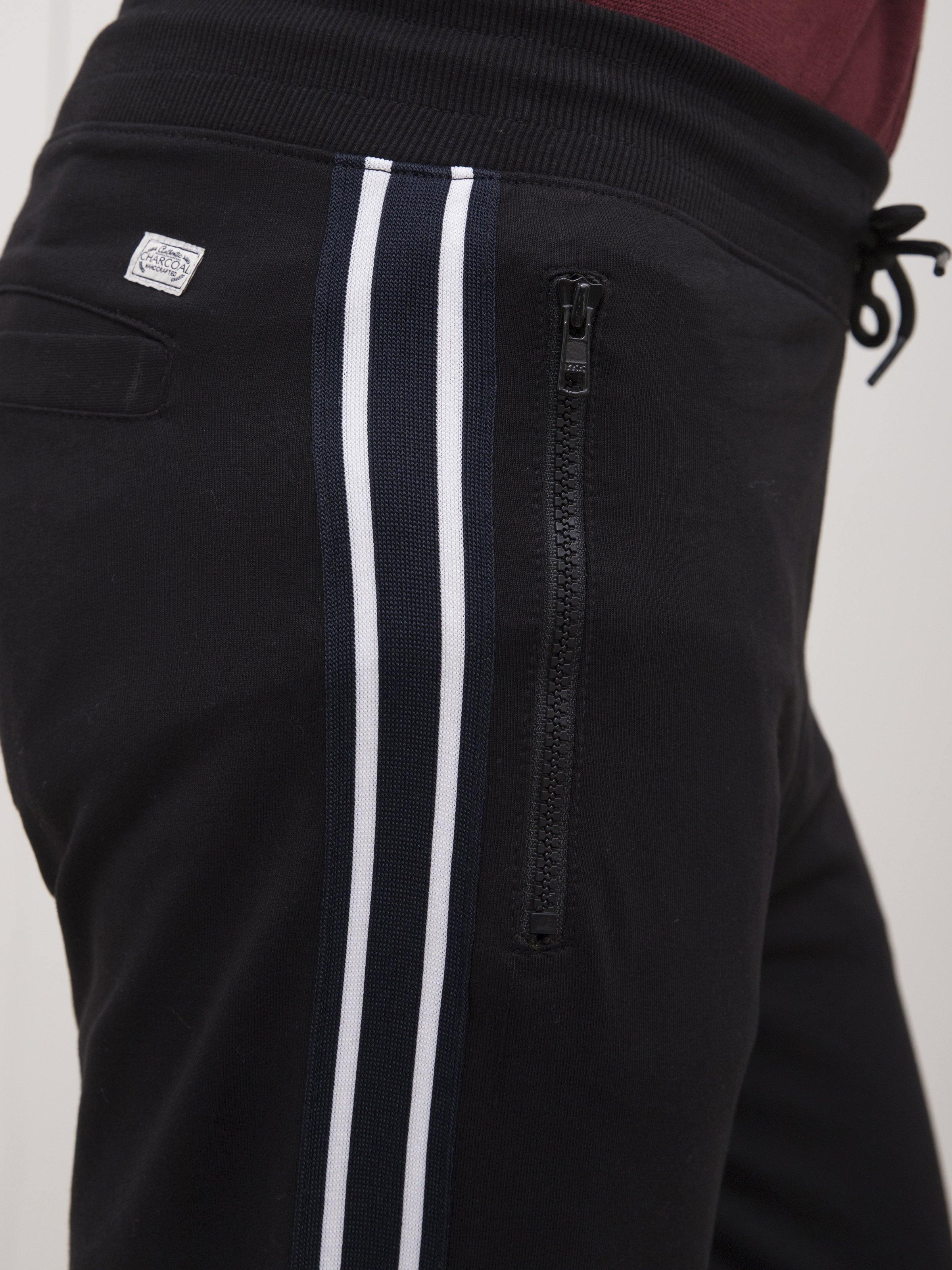 Black trouser leg close-up with white twin stripe and zip pocket detail