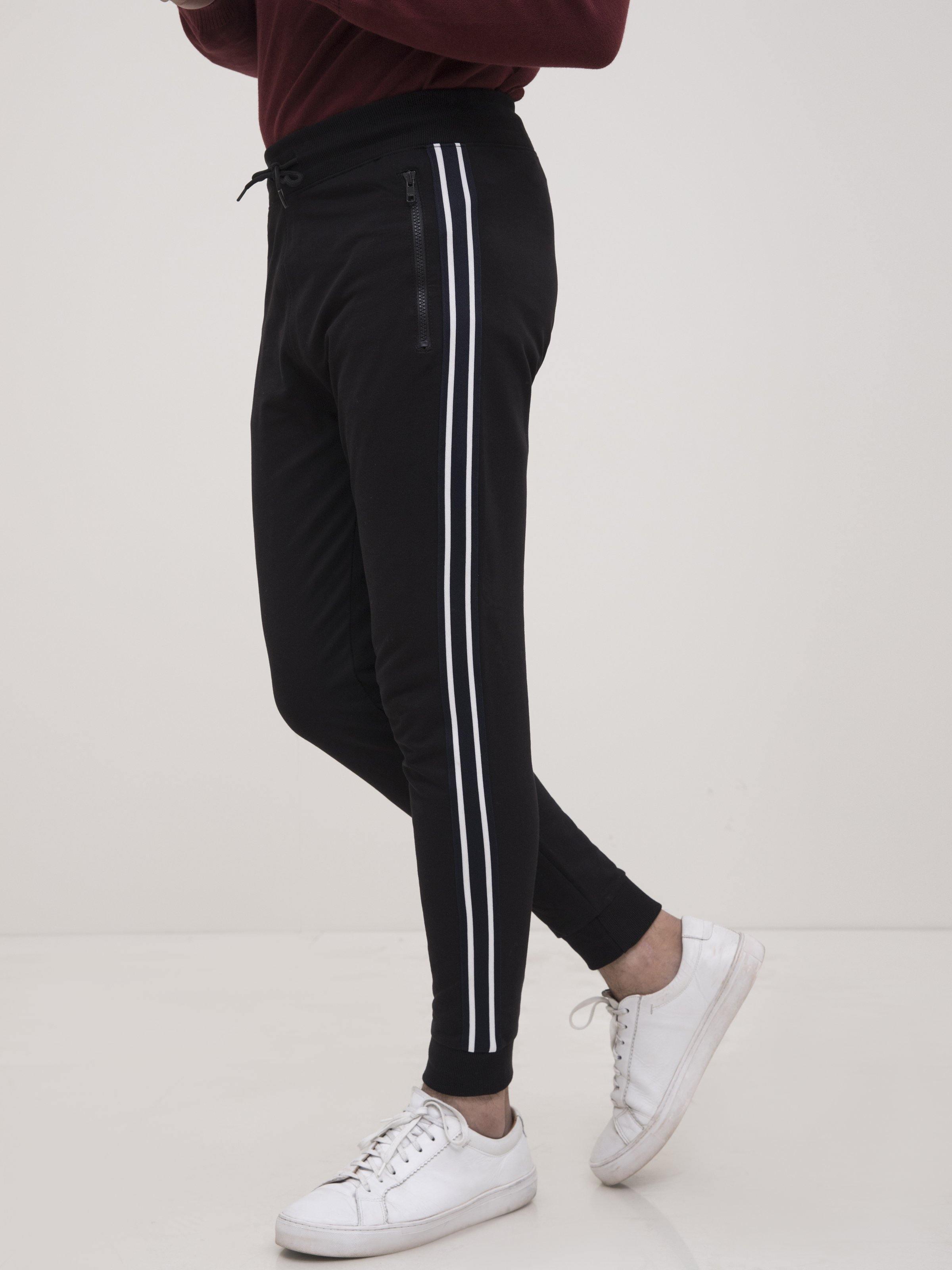 Black track-style trousers with white side tape stripes and cuffed ankle