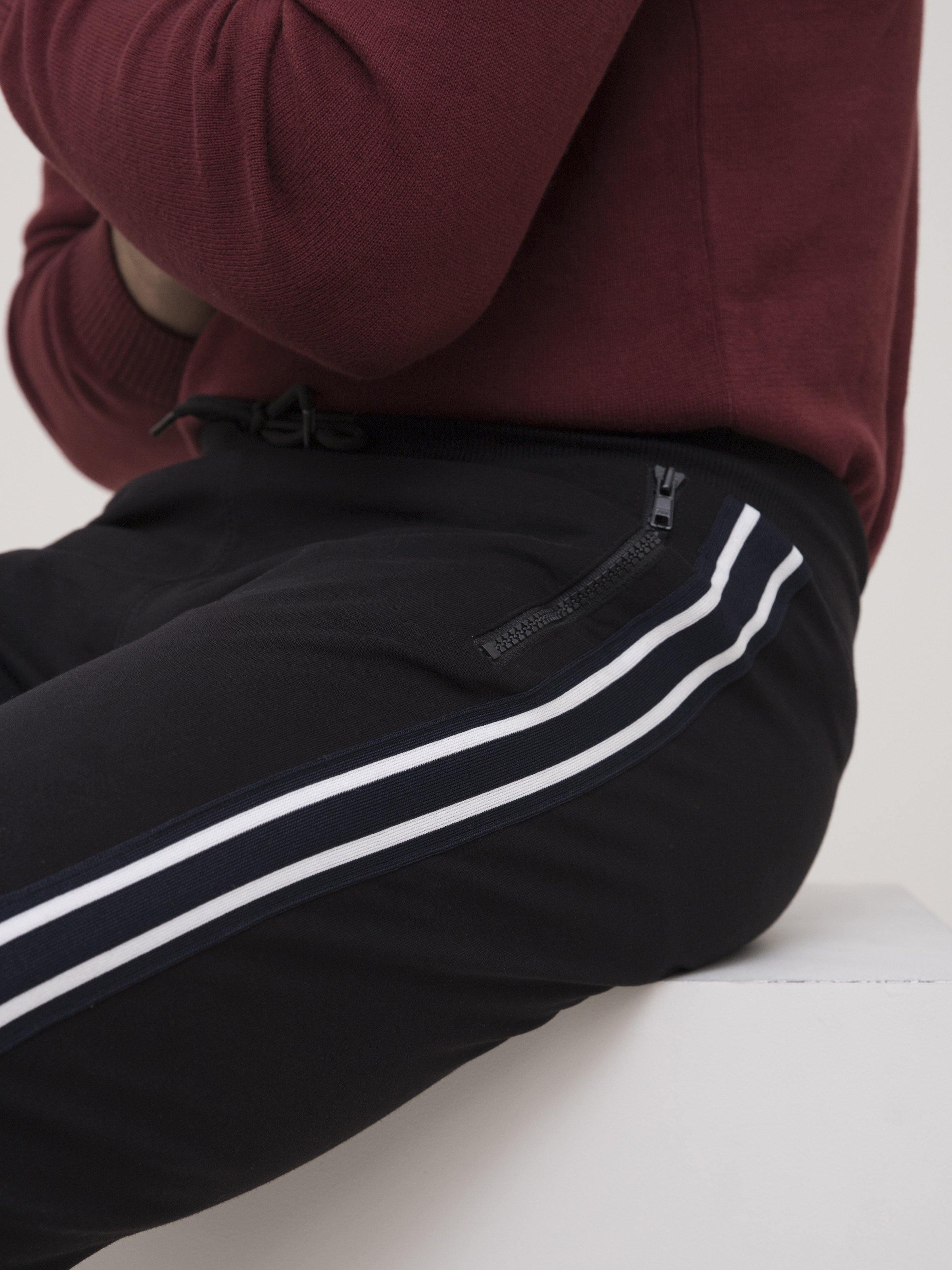 Black track trousers close-up with white side stripes and zip fly opening