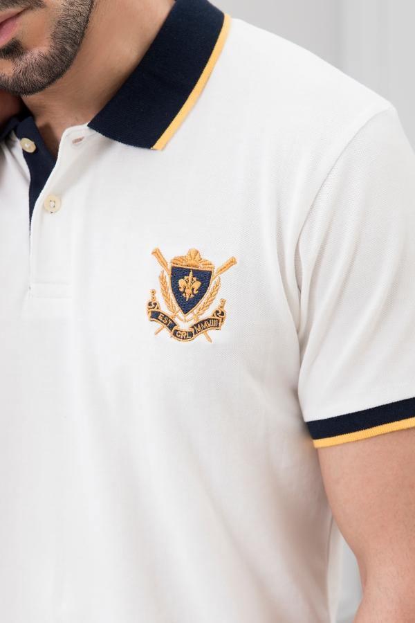 White polo shirt close-up with navy collar trim and embroidered crest on chest