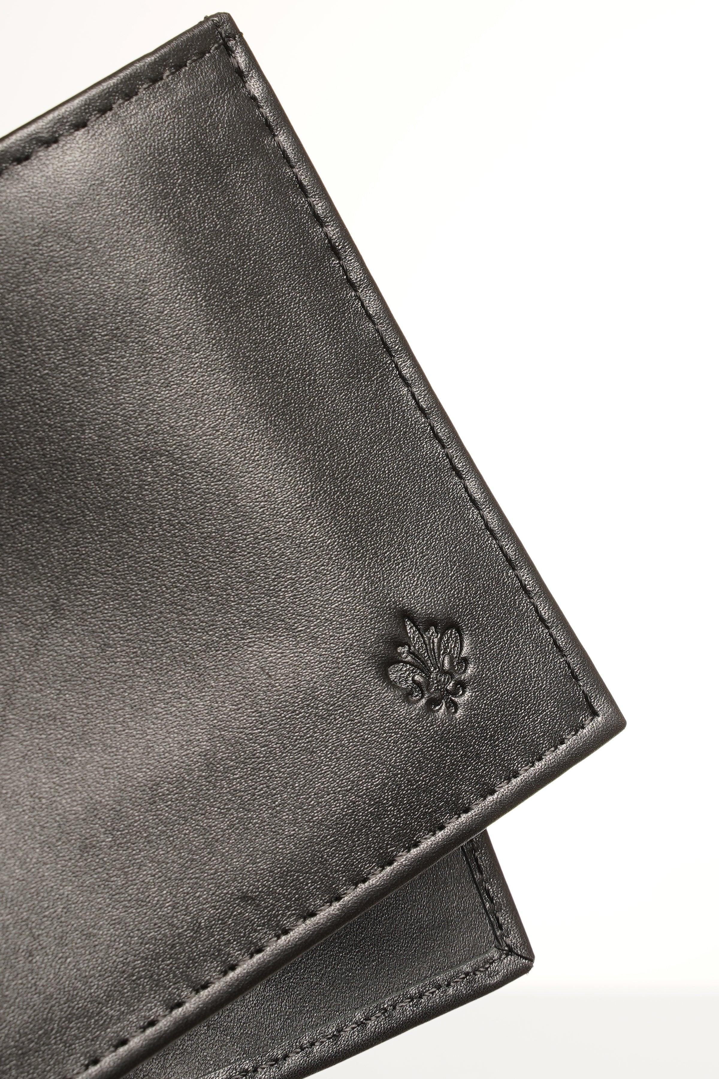 Black leather wallet corner with embossed clover emblem and stitched seam.