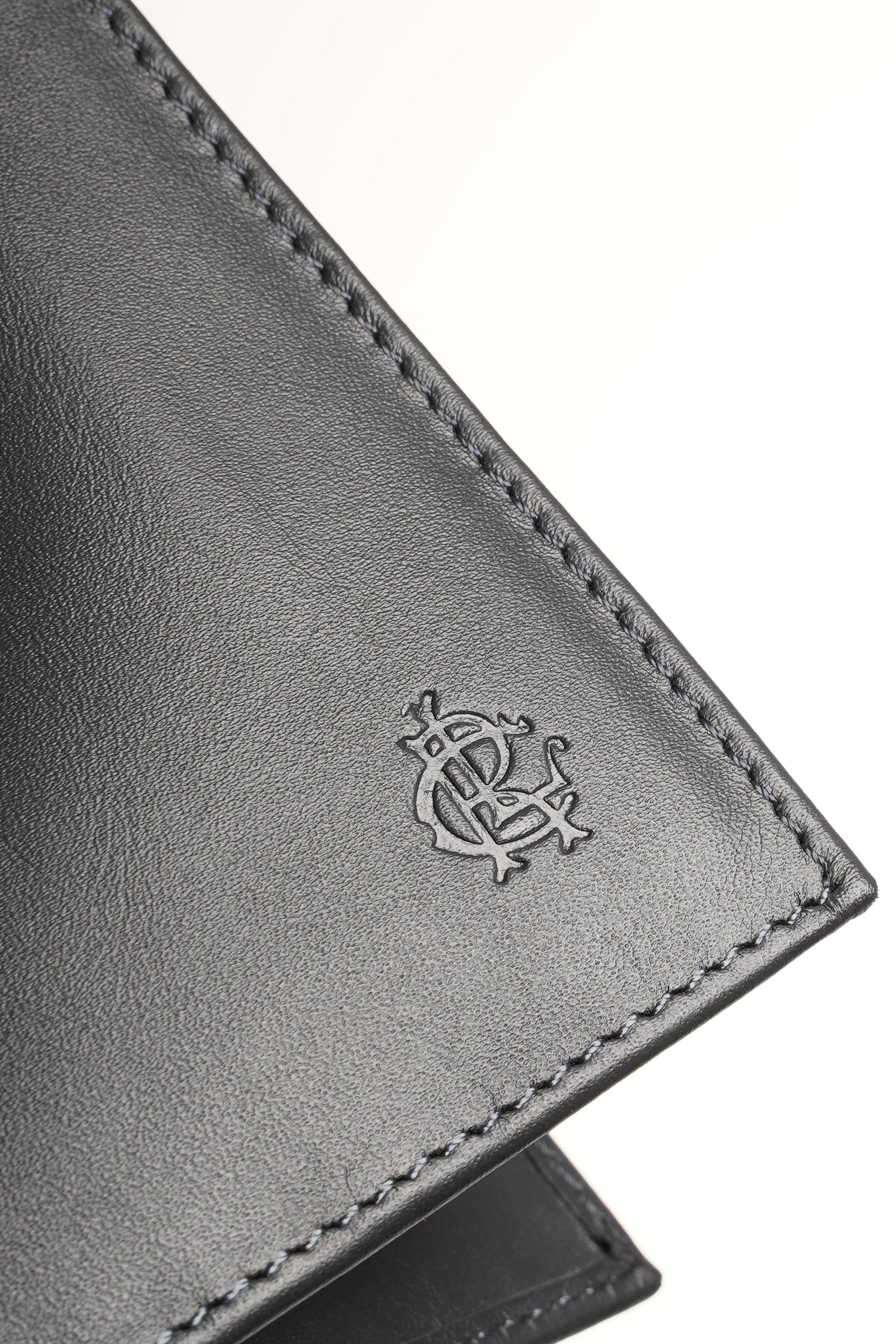 Dark leather wallet corner with embossed logo and visible edge stitching.