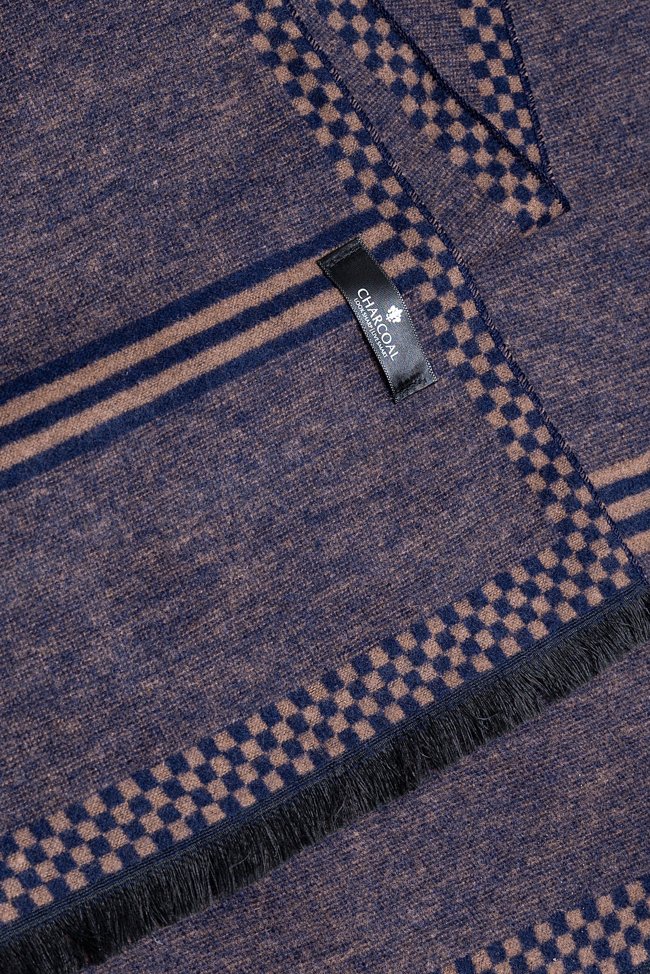 Scarf close-up: woven plaid pattern with brand label and dark fringe edge
