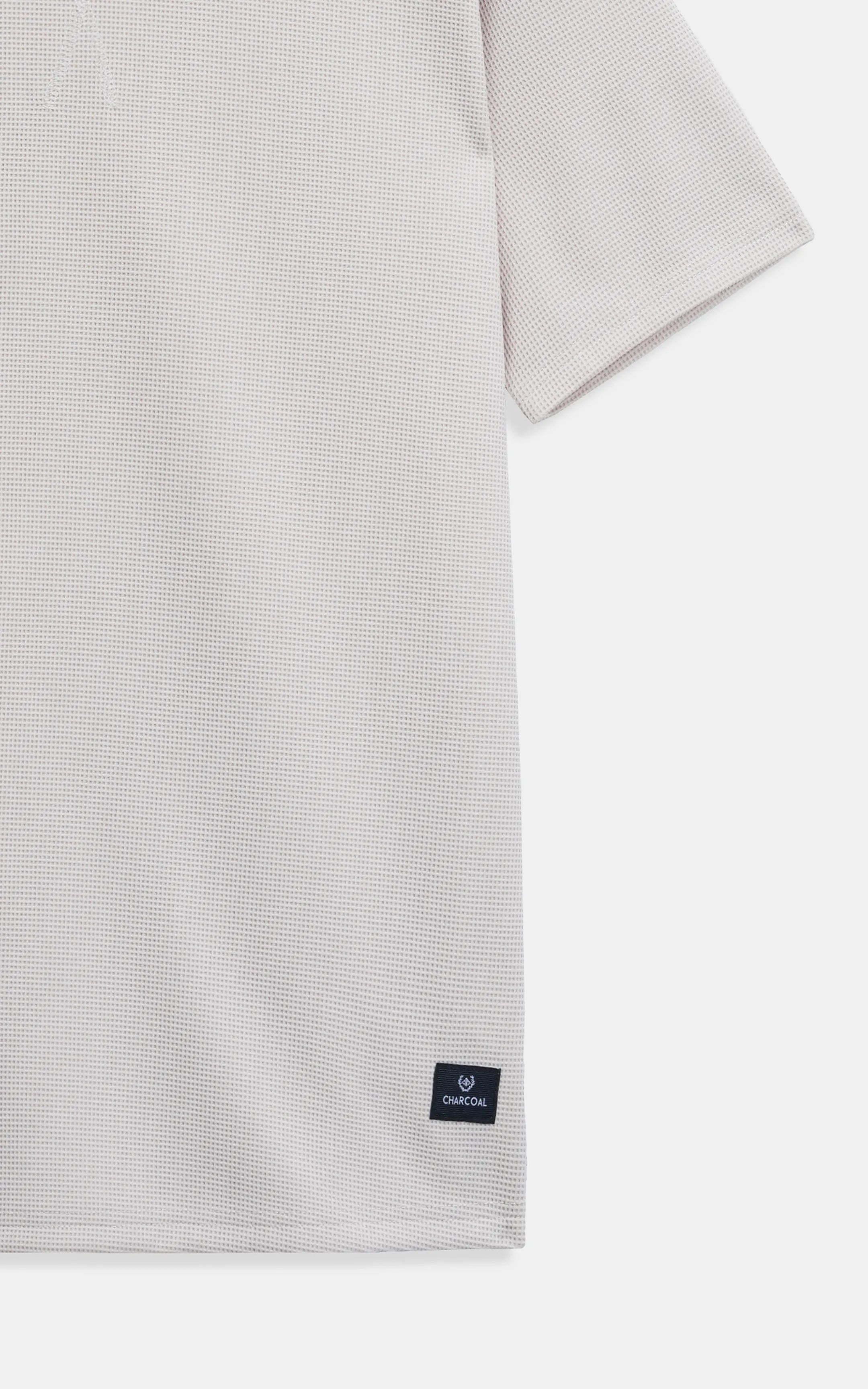 Beige textured T-shirt with small square logo patch at lower front hem