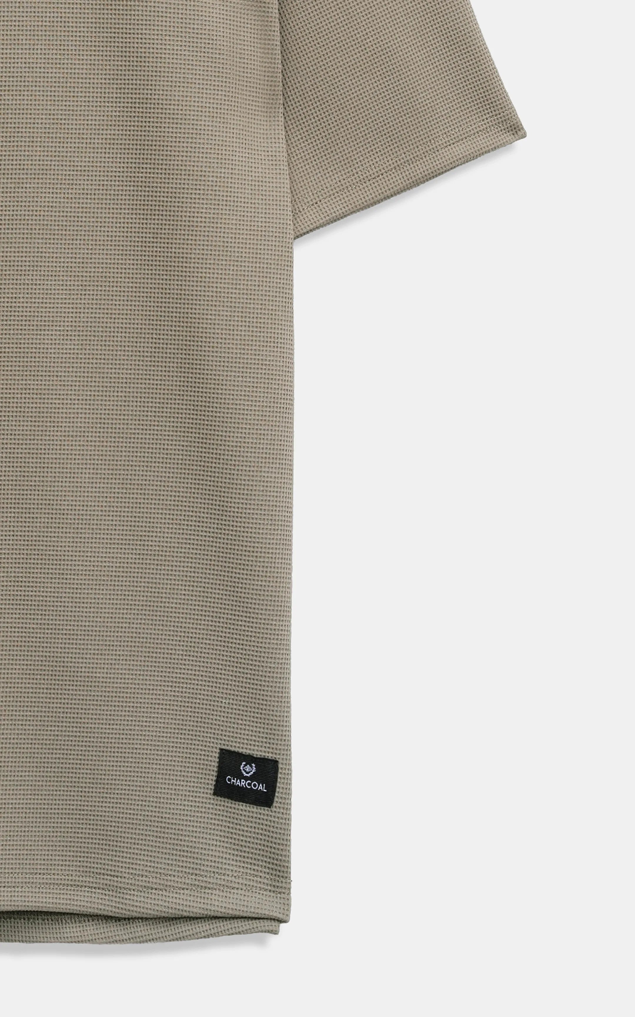 Oversized T-shirt hem with small brand patch detail, muted green fabric