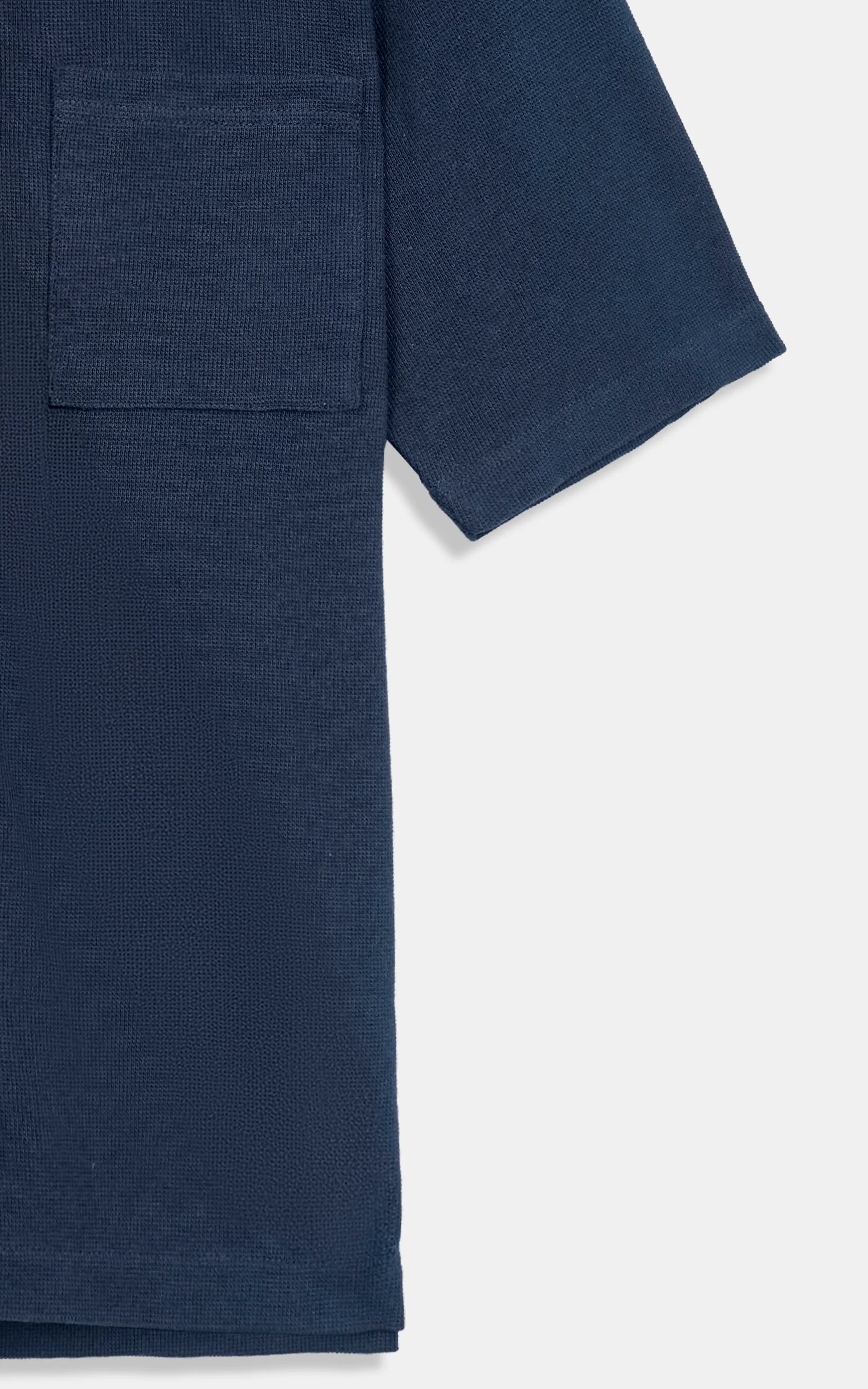 Navy knit shirt close-up of chest pocket and short-sleeve hem detail.