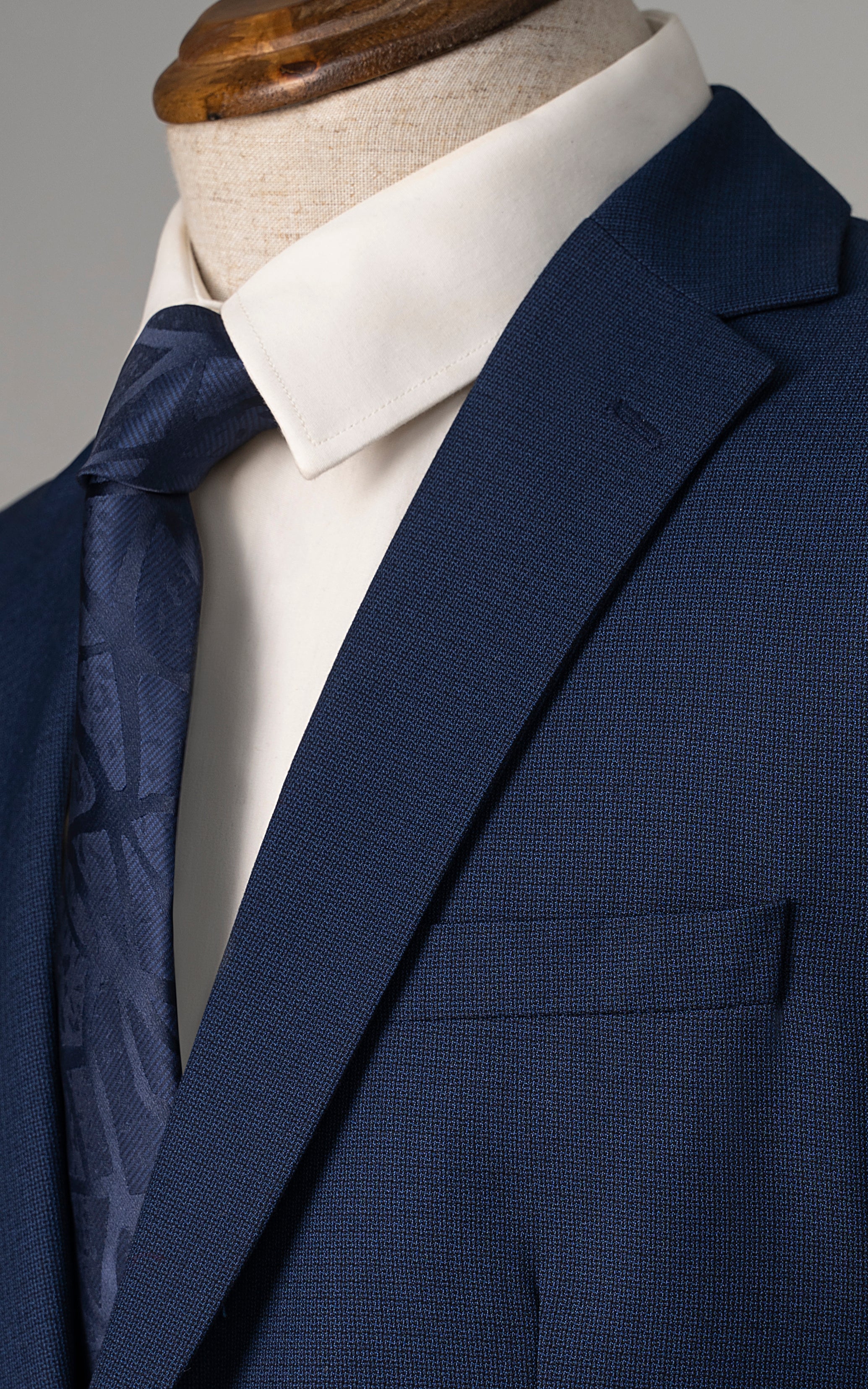 Blue suit jacket close-up with notch lapel, front pocket, and white shirt collar
