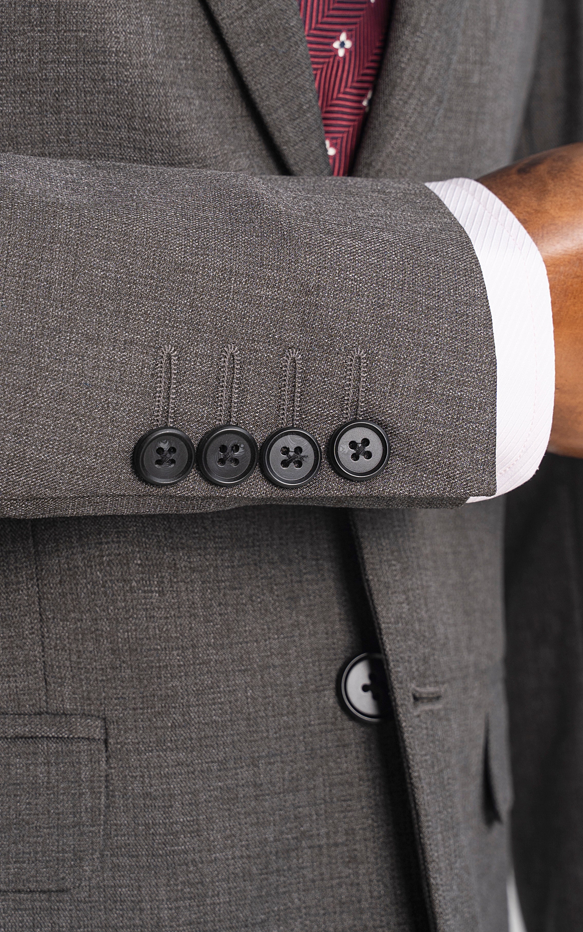 Grey suit jacket cuff and button details with maroon tie visible