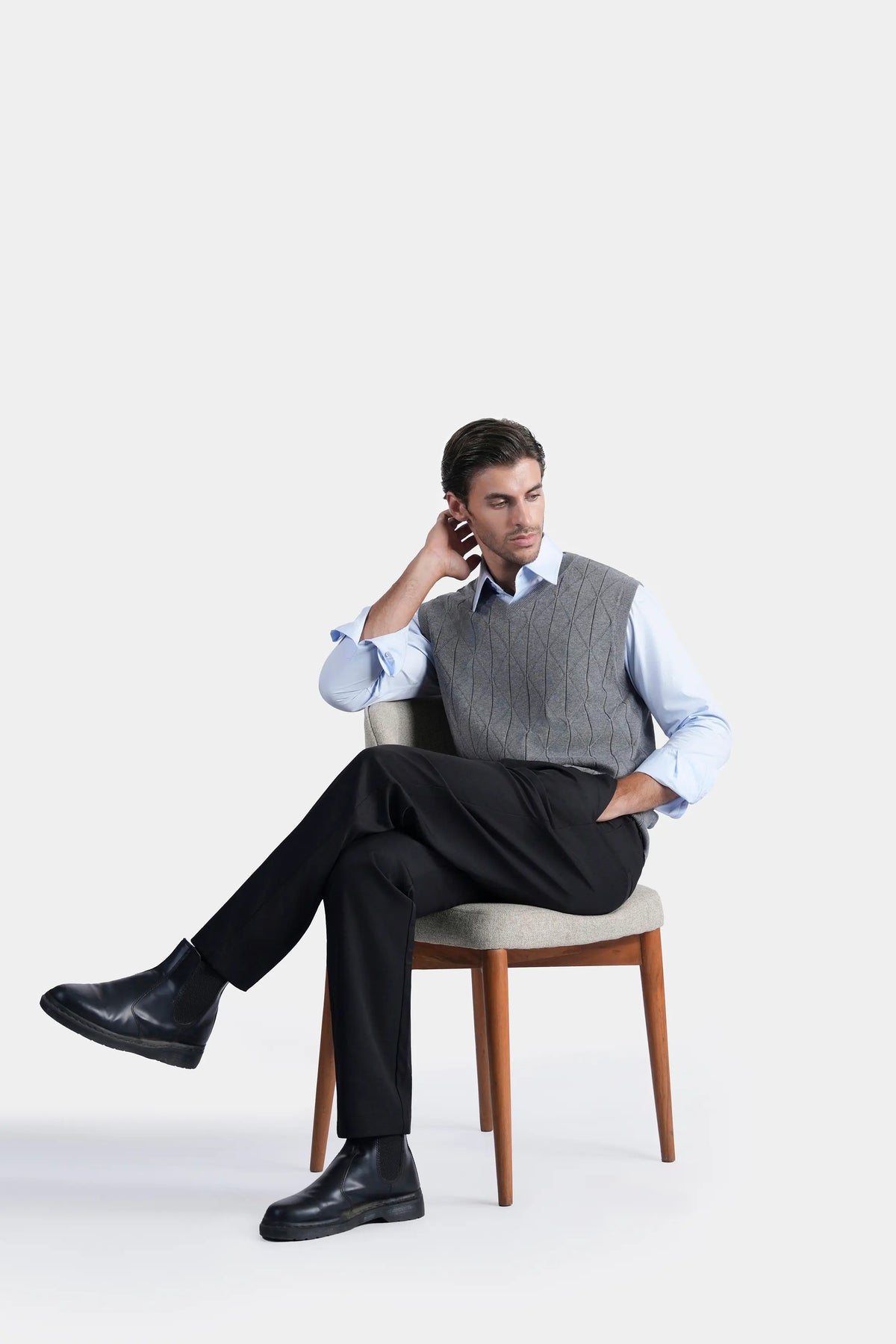 Grey sleeveless knitted V-neck sweater vest, worn in seated pose with detailed knit texture