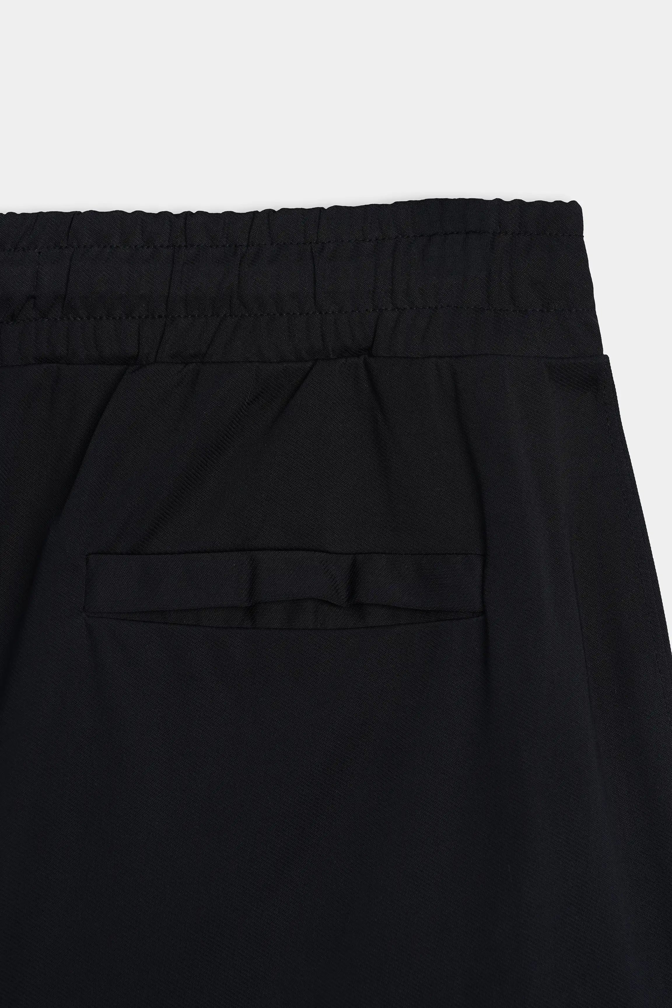 Black trousers close-up showing gathered elastic waistband and centered front pleat