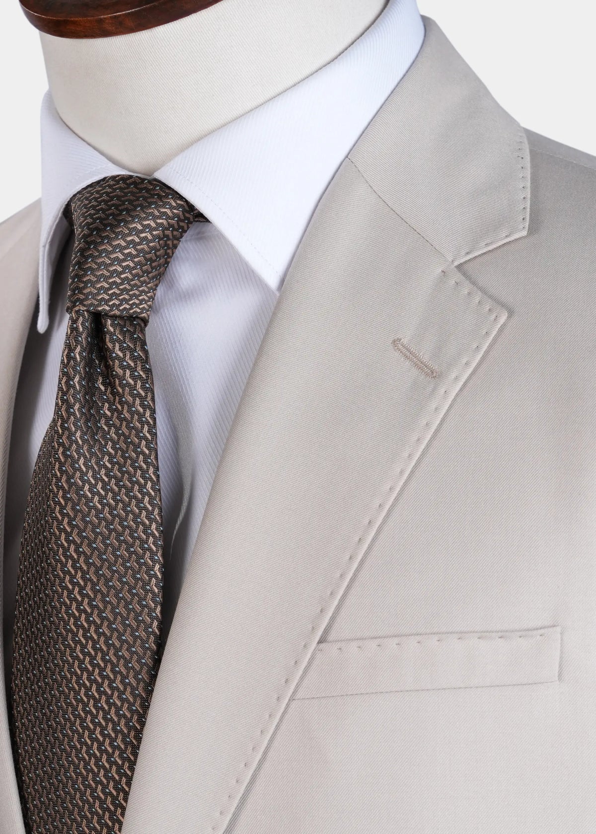 Cream suit jacket detail: notch lapel, flap pocket, patterned tie and white shirt