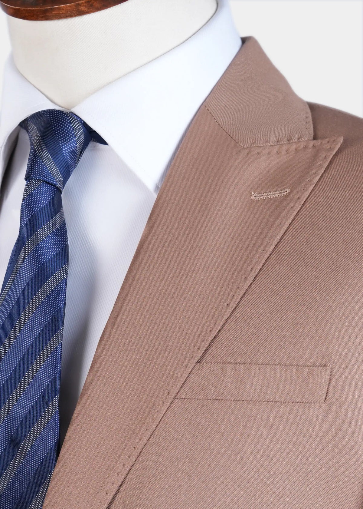 Close-up of light brown suit jacket with flap pocket detail and blue striped tie.