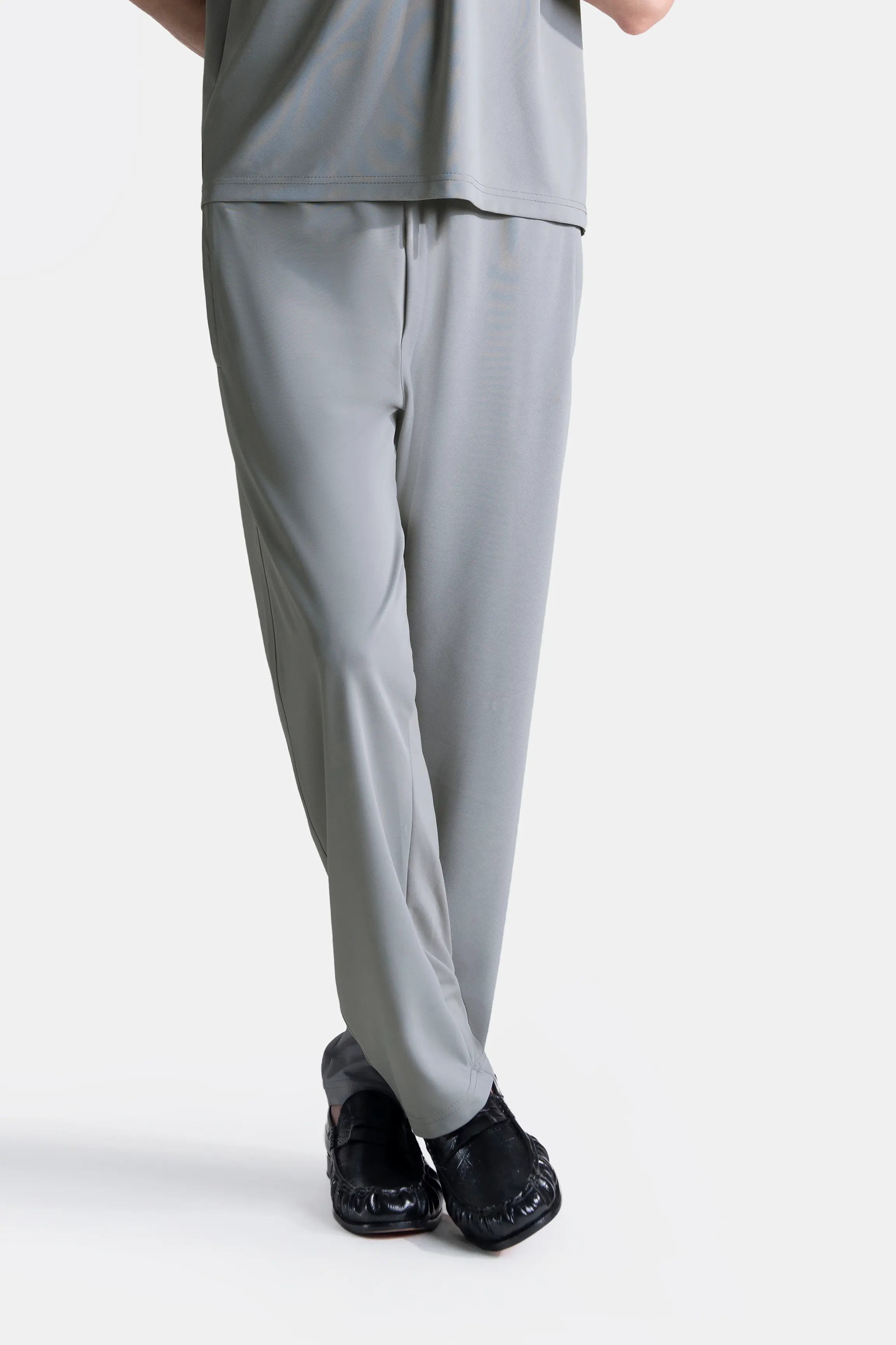 Grey loose-fit trousers with elasticated waistband, cuffed hem, side view near shoes.