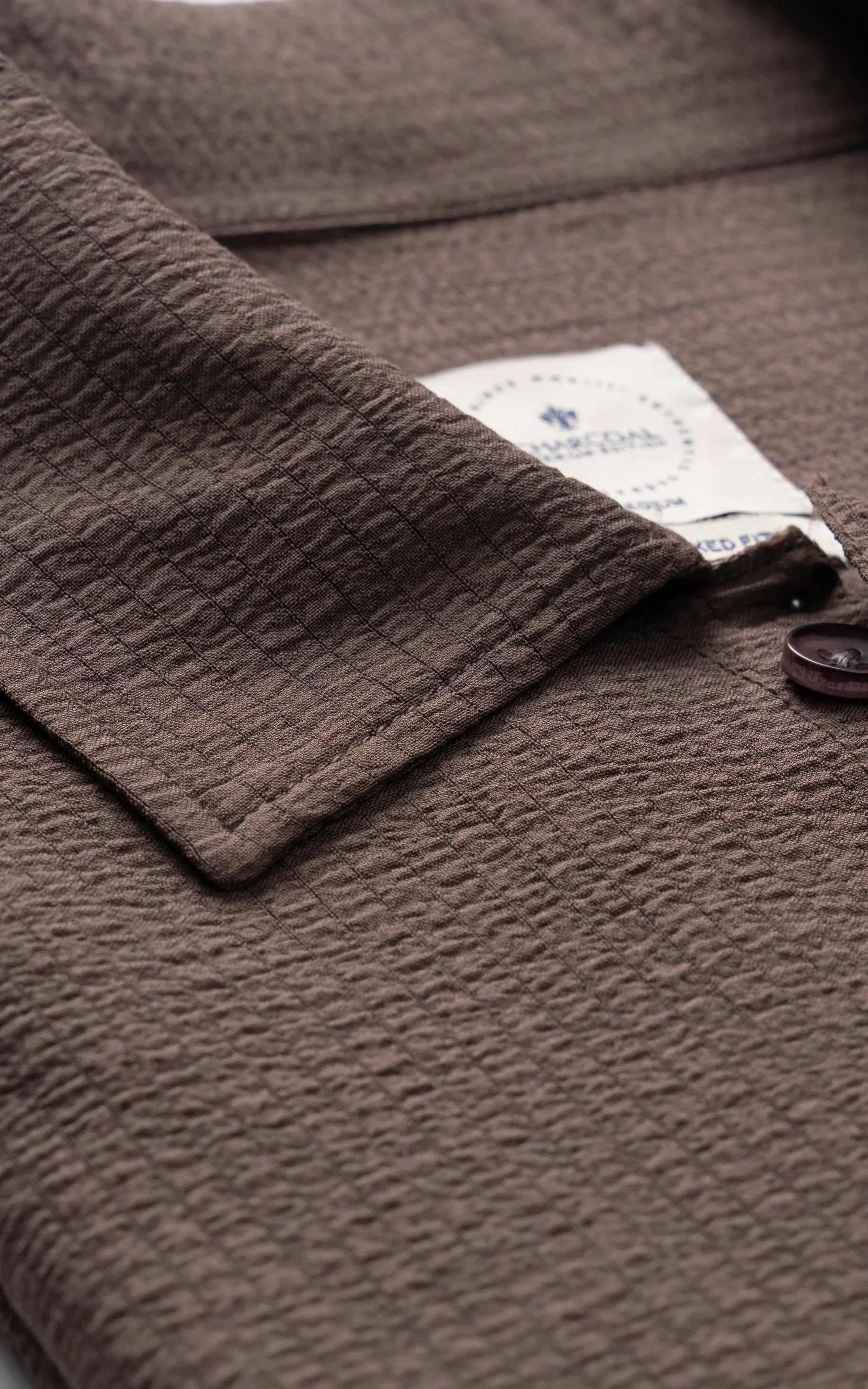 Brown shirt collar close-up with dark buttons and brand label on placket